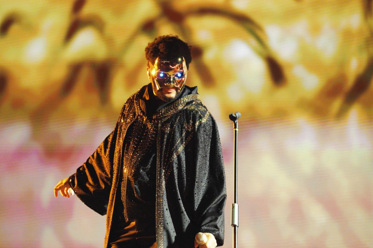 A close up of a singer in a mask stands onstage and looks down.
