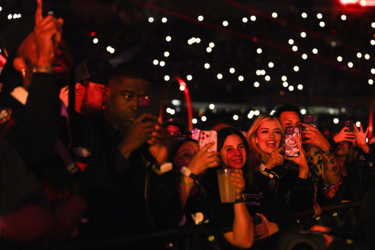 The audience members hold up their phones and smile towards the stage.
