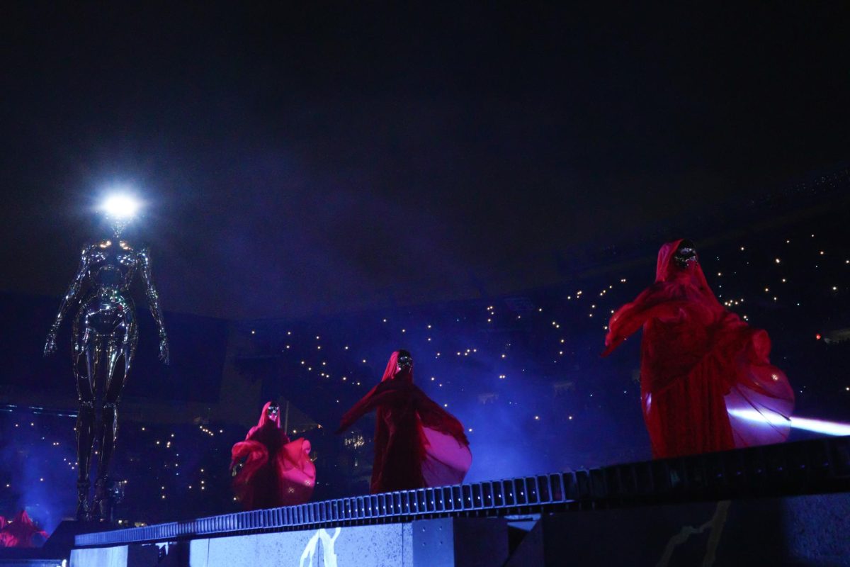 A wide shot of backup dancers standing onstage with the audience in the background.